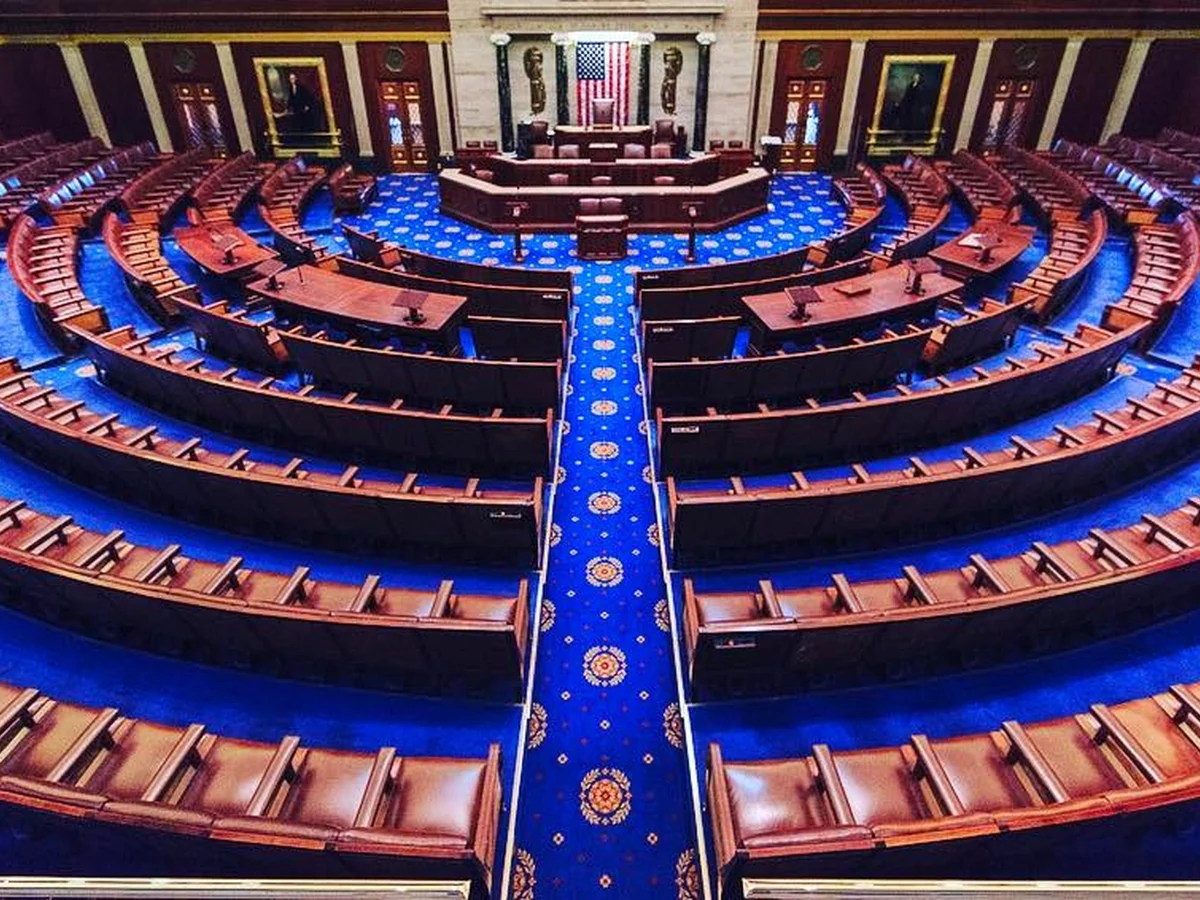 Empty U.S. House chamber viewed from the gallery, with the Speaker’s rostrum and voting boards visible.