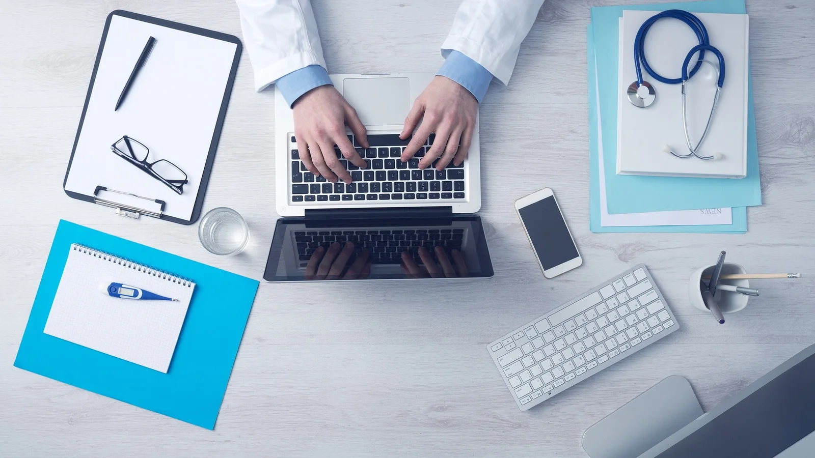 Computer, keyboard, stethoscope and medical forms arranged on a clinician's desk.