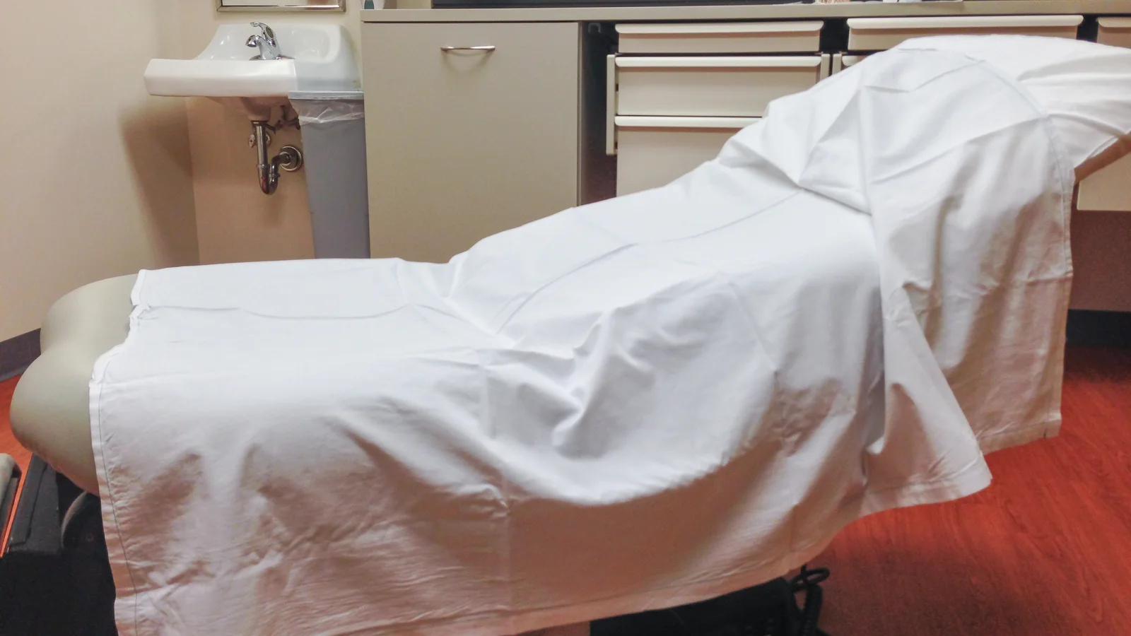 Medical exam room with an examination table, chair, counter and clinical equipment.