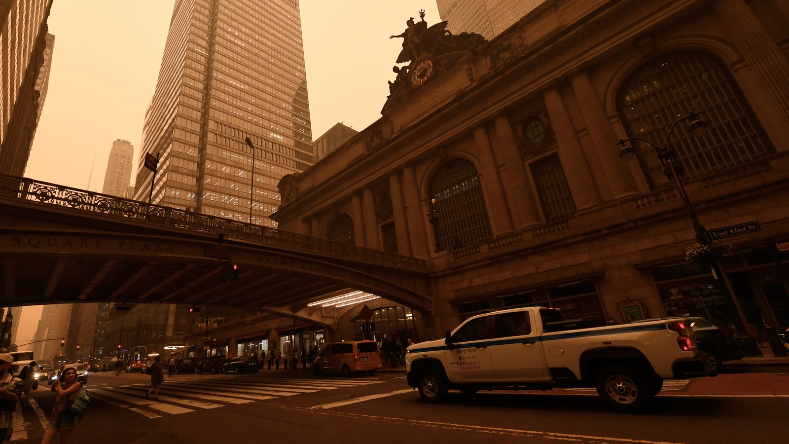 Heavy wildfire smoke turns the sky orange above traffic and pedestrians on a Manhattan street.