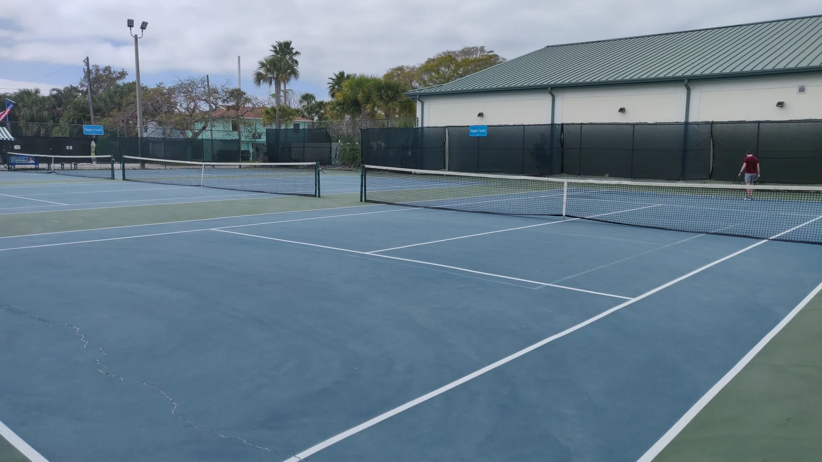Several blue and green outdoor tennis courts viewed from above the surrounding fence.