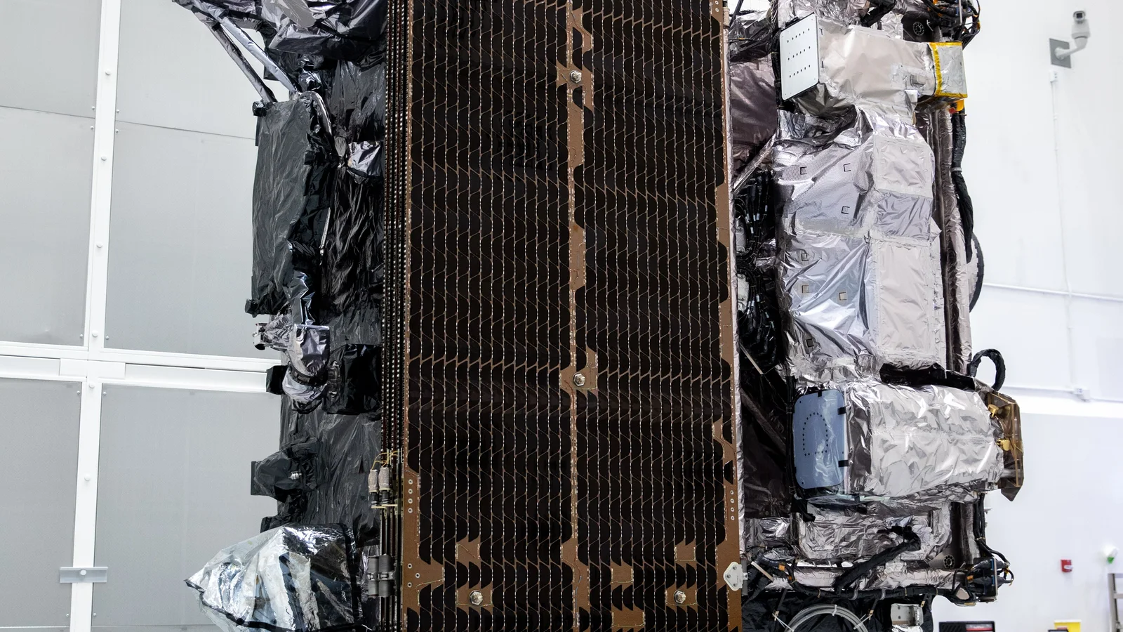 A large Earth-observing satellite standing inside a brightly lit spacecraft cleanroom.