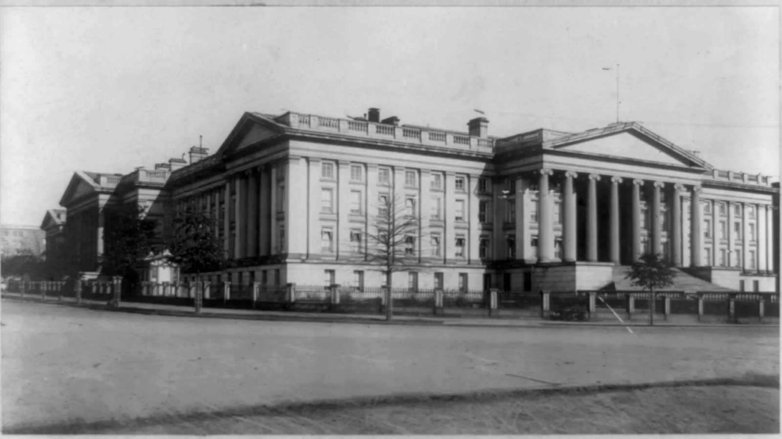A historic view of the United States Treasury Building and its long colonnade beside a broad Washington street.