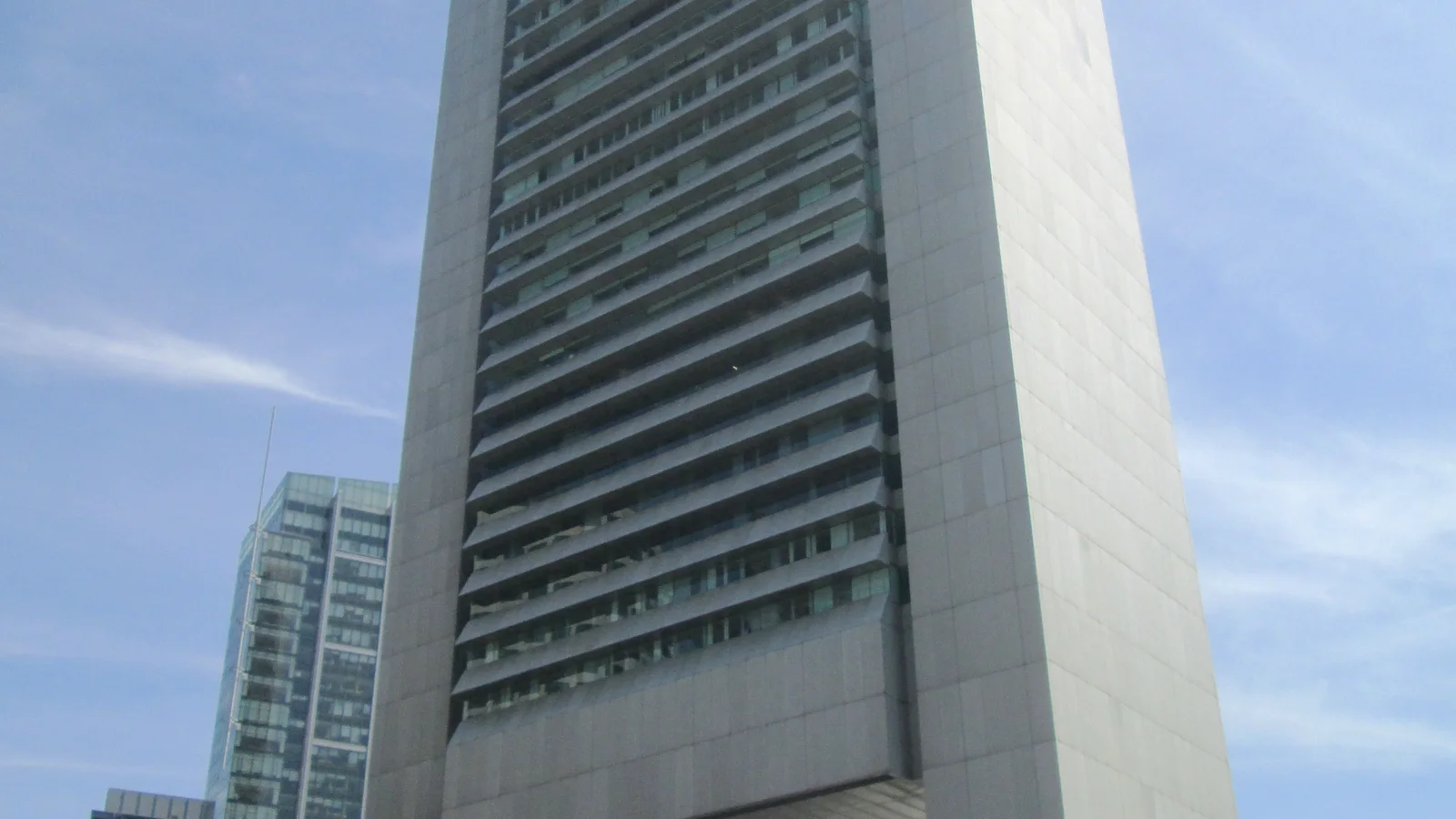 The tall concrete Federal Reserve Bank of Boston tower rises above a downtown intersection under a blue sky.