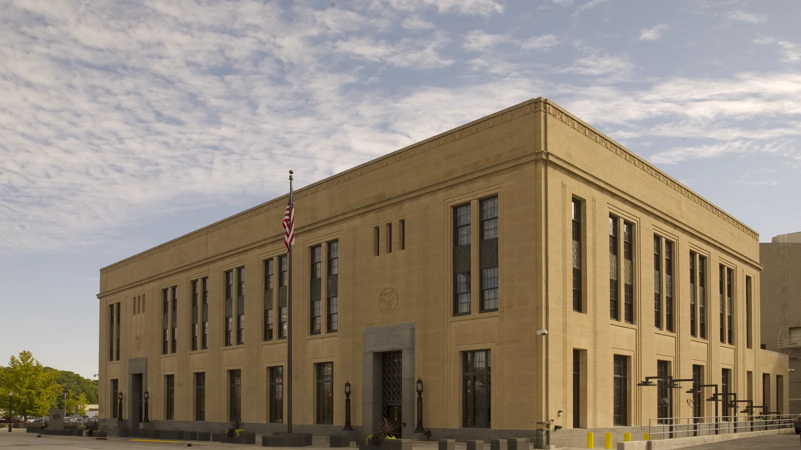 A broad stone United States courthouse with tall columns and steps on a sunny street corner in Davenport, Iowa.