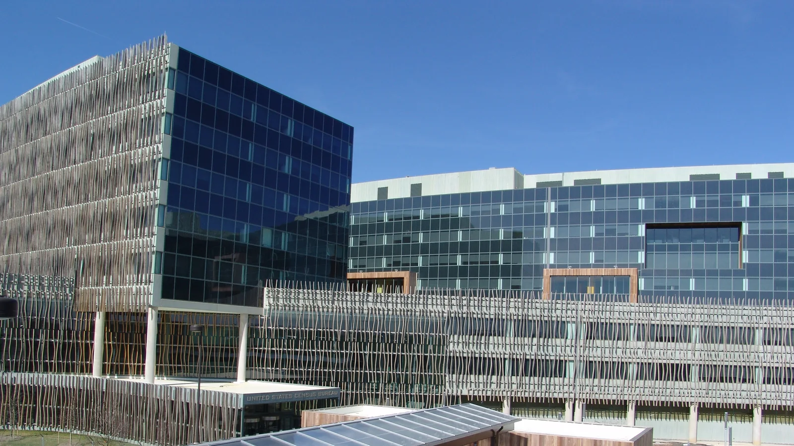 The glass-and-wood facade of the United States Census Bureau headquarters curves beside a landscaped plaza.