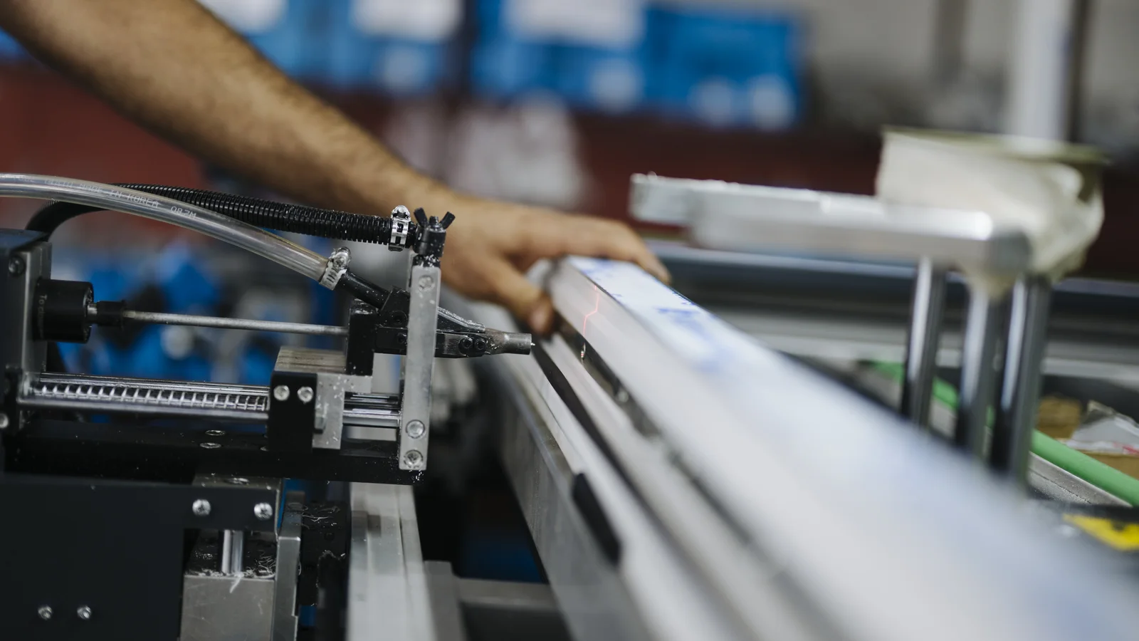 A worker's arm reaches across precision machinery on a factory production line.