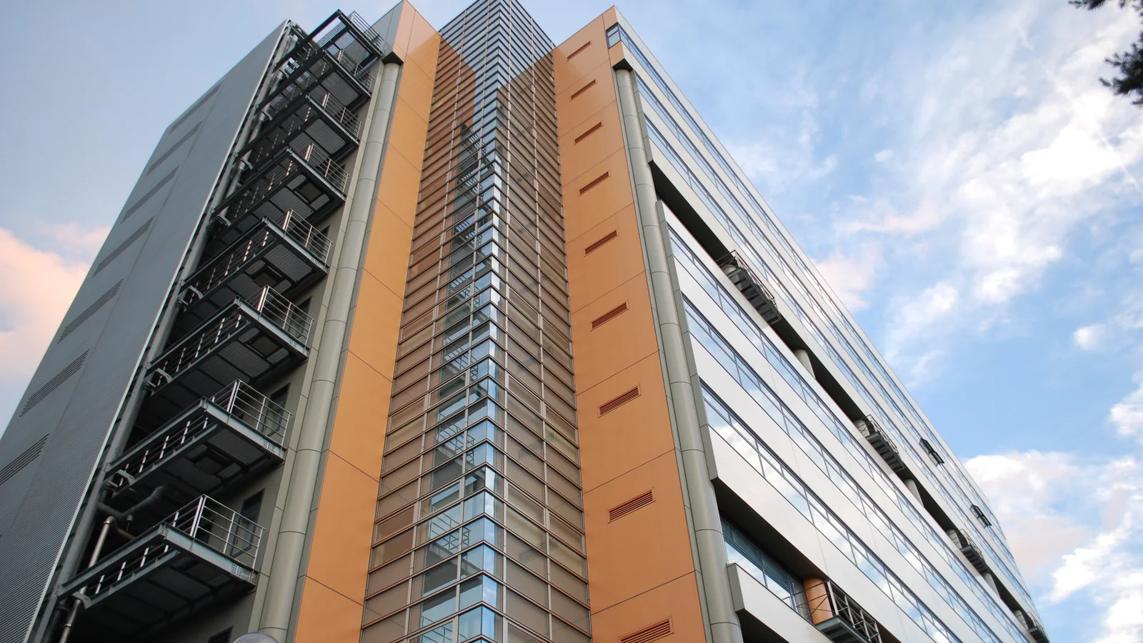 A tall modern university research building rises against a blue and clouded sky.