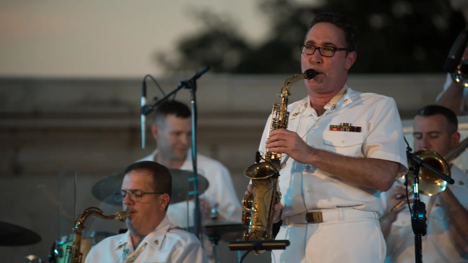 A large jazz ensemble performs on an outdoor stage with brass, woodwind and rhythm sections.