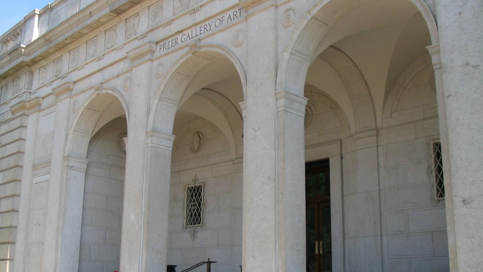 The stone facade and arched entrances of the Freer Gallery face a landscaped walkway.