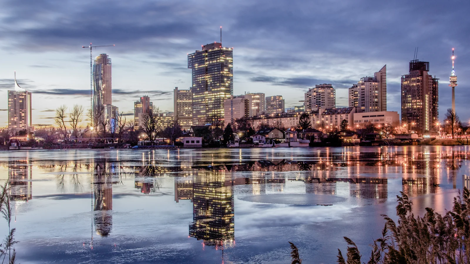 Vienna's modern skyline reflects in calm water beneath a pale winter sky.