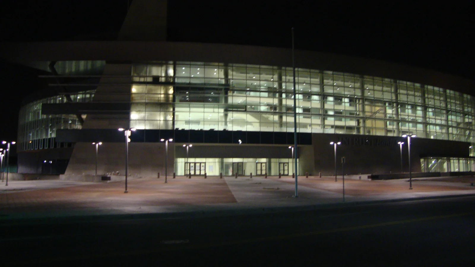 A brightly lit indoor arena with a curved glass entrance stands against the night sky in Wichita.