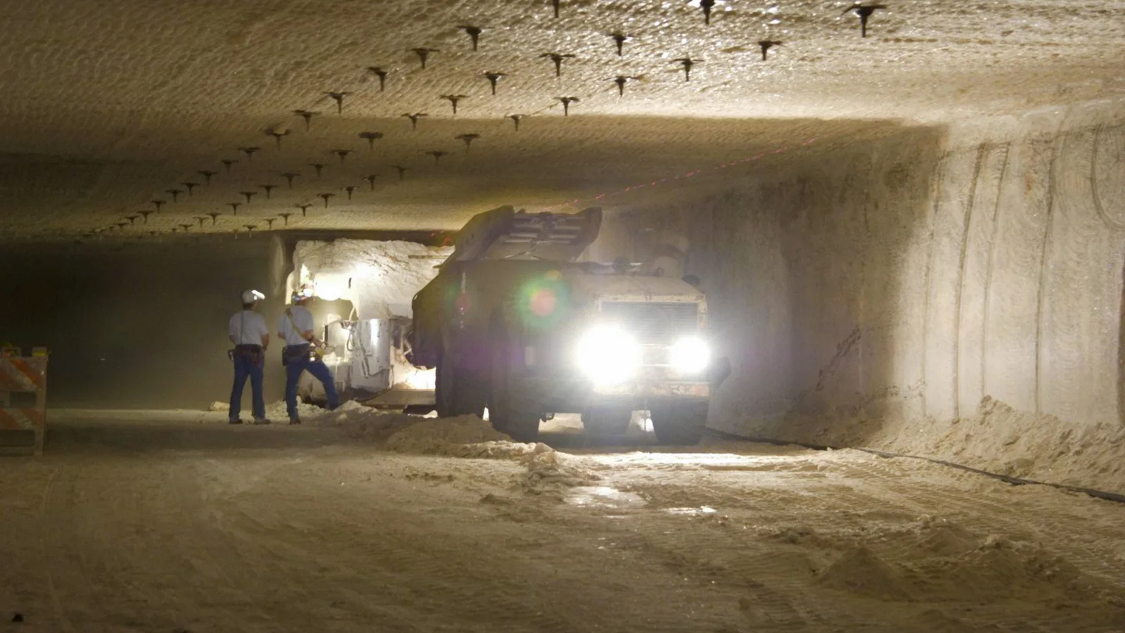 A worker and industrial equipment stand in a broad underground salt chamber used for nuclear waste disposal.