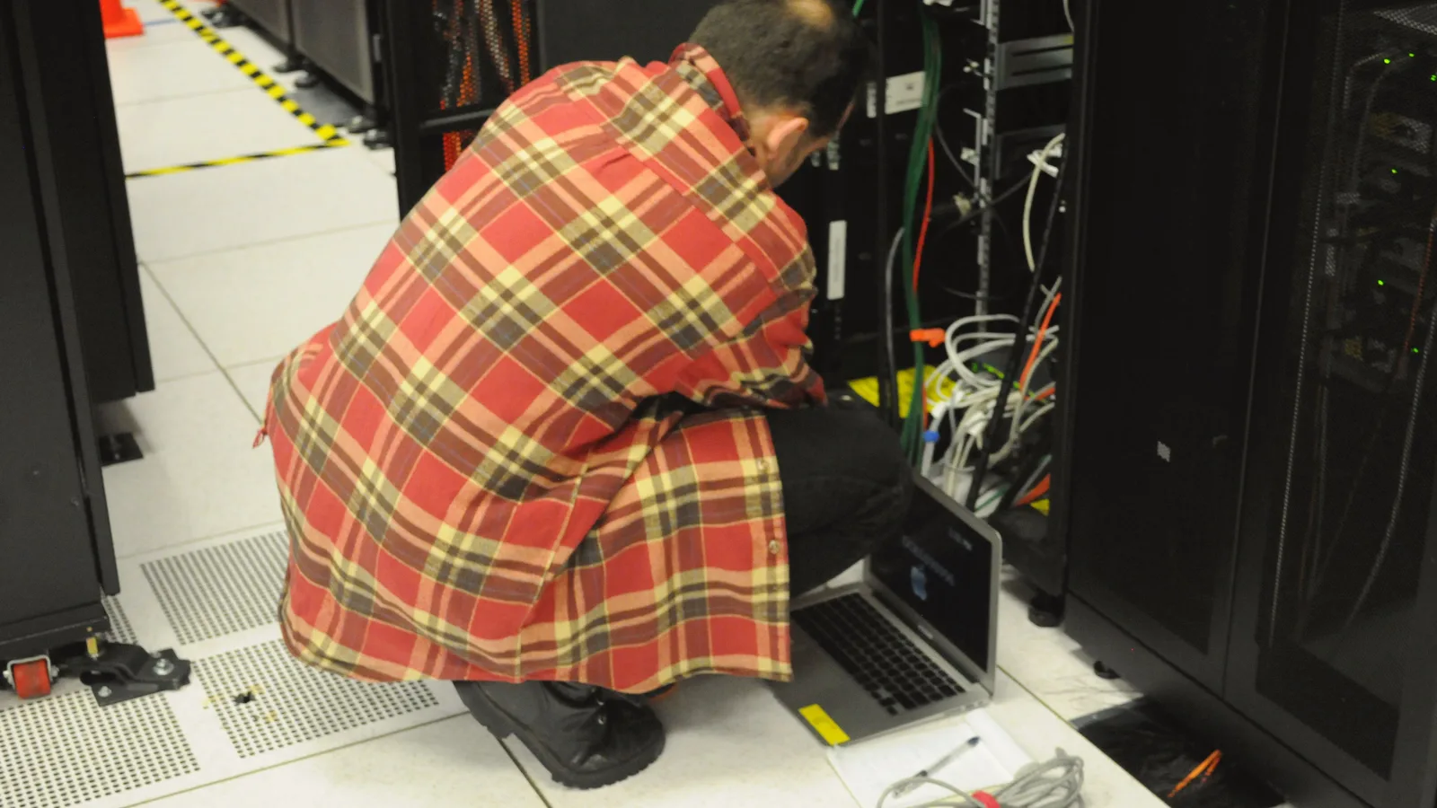A technician uses a laptop beside tall server racks in a computing center.