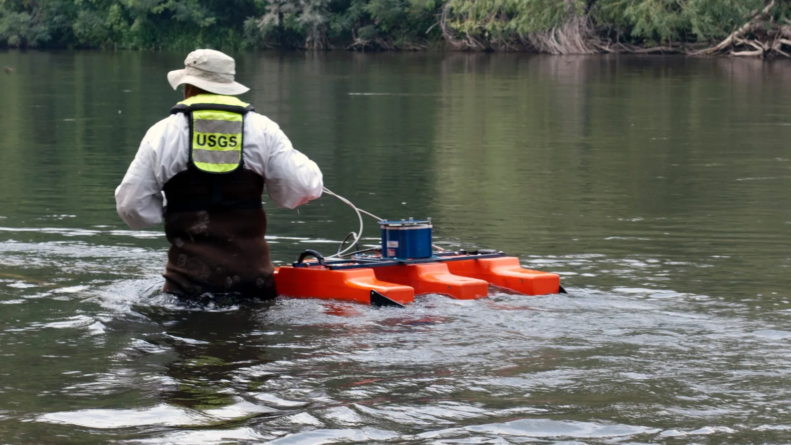 A hydrologic technician in a small boat measures the flow of a broad river.