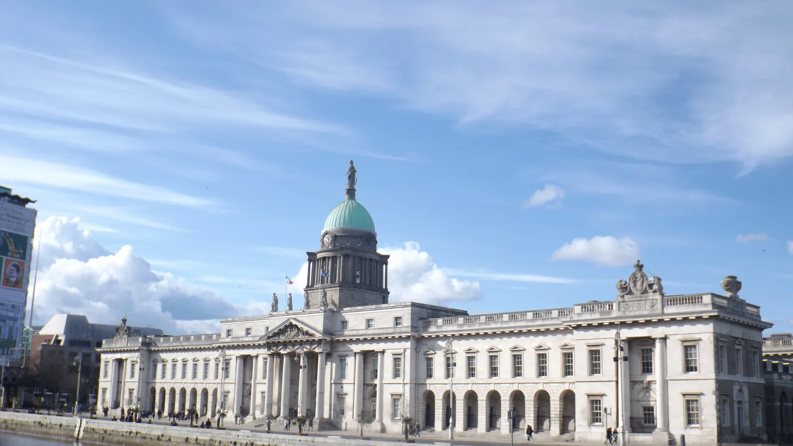 Dublin's domed Custom House stands beside the River Liffey under a blue sky.