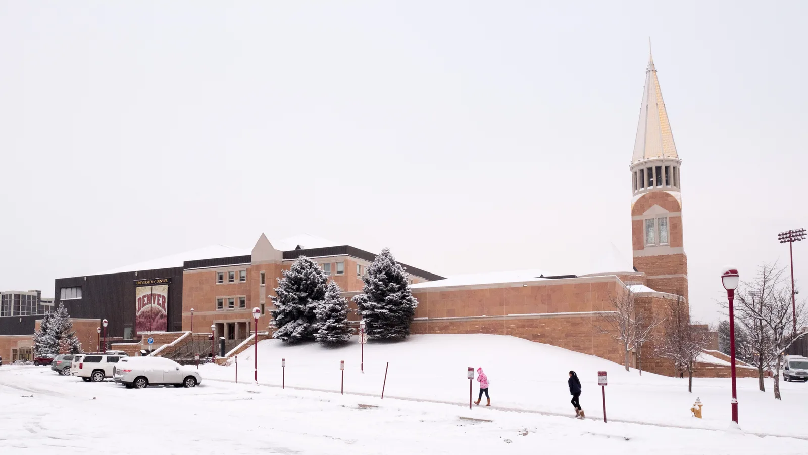 A snow-covered college sports arena and campus tower stand beneath an overcast winter sky.