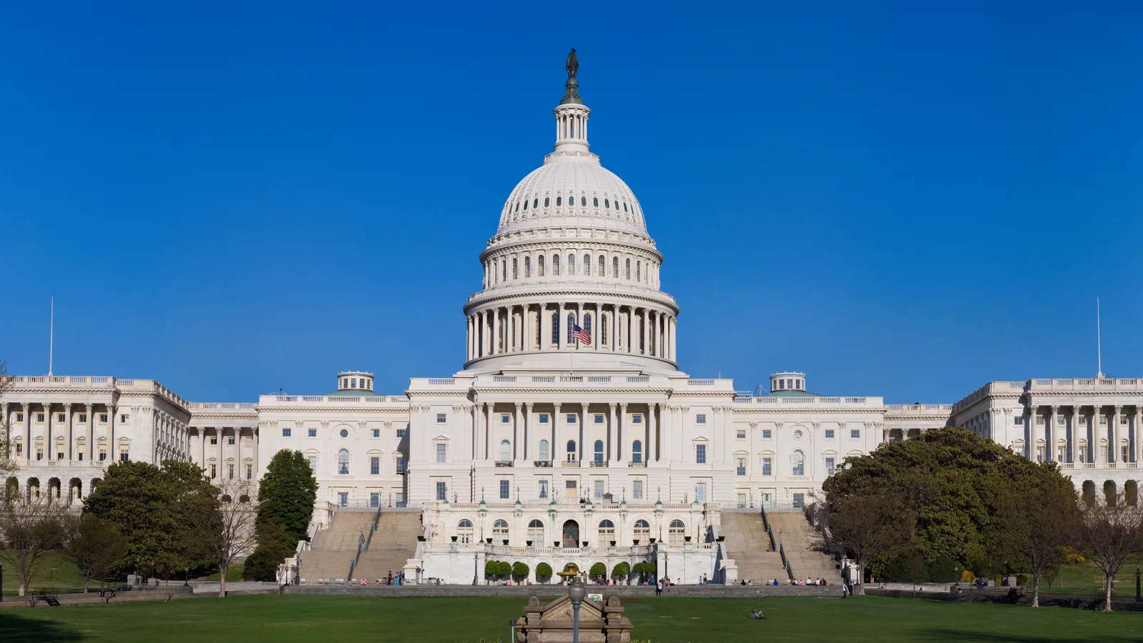 The U.S. Capitol dome and western steps rise behind a broad lawn beneath a blue sky.
