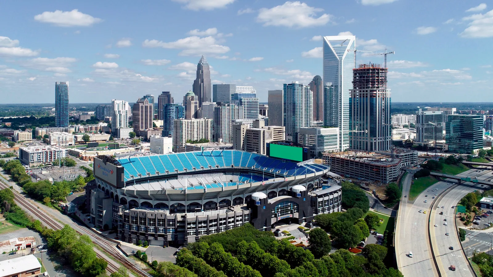 Charlotte's skyline rises beyond neighborhoods and tree-lined streets in a wide aerial view.
