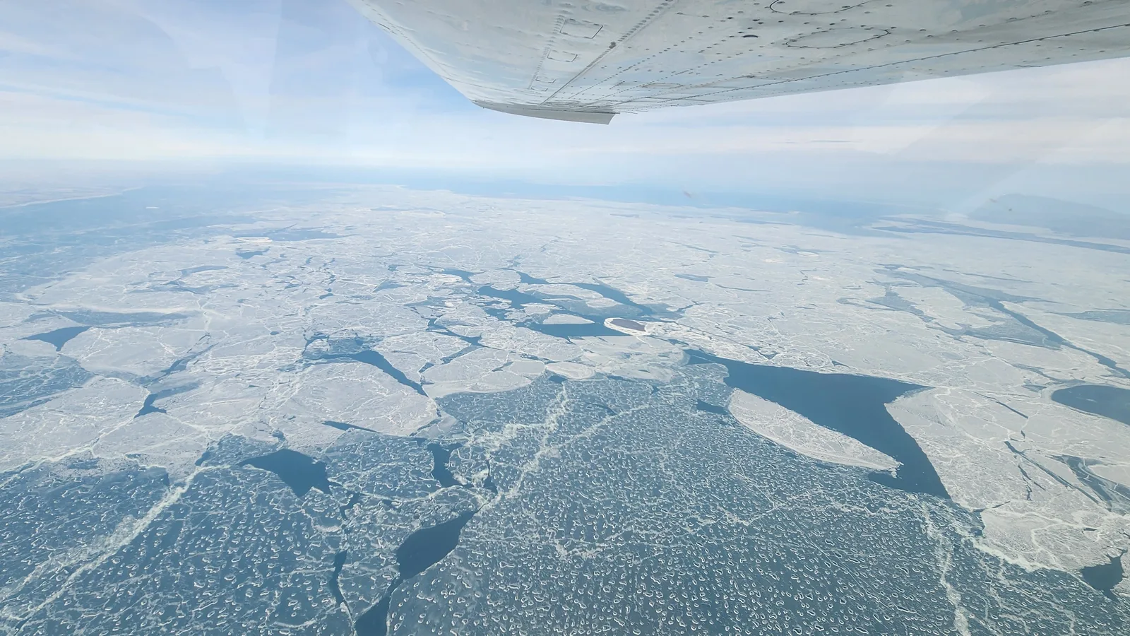 Broken white ice sheets and dark open water stretch across Lake Erie beneath a research aircraft.