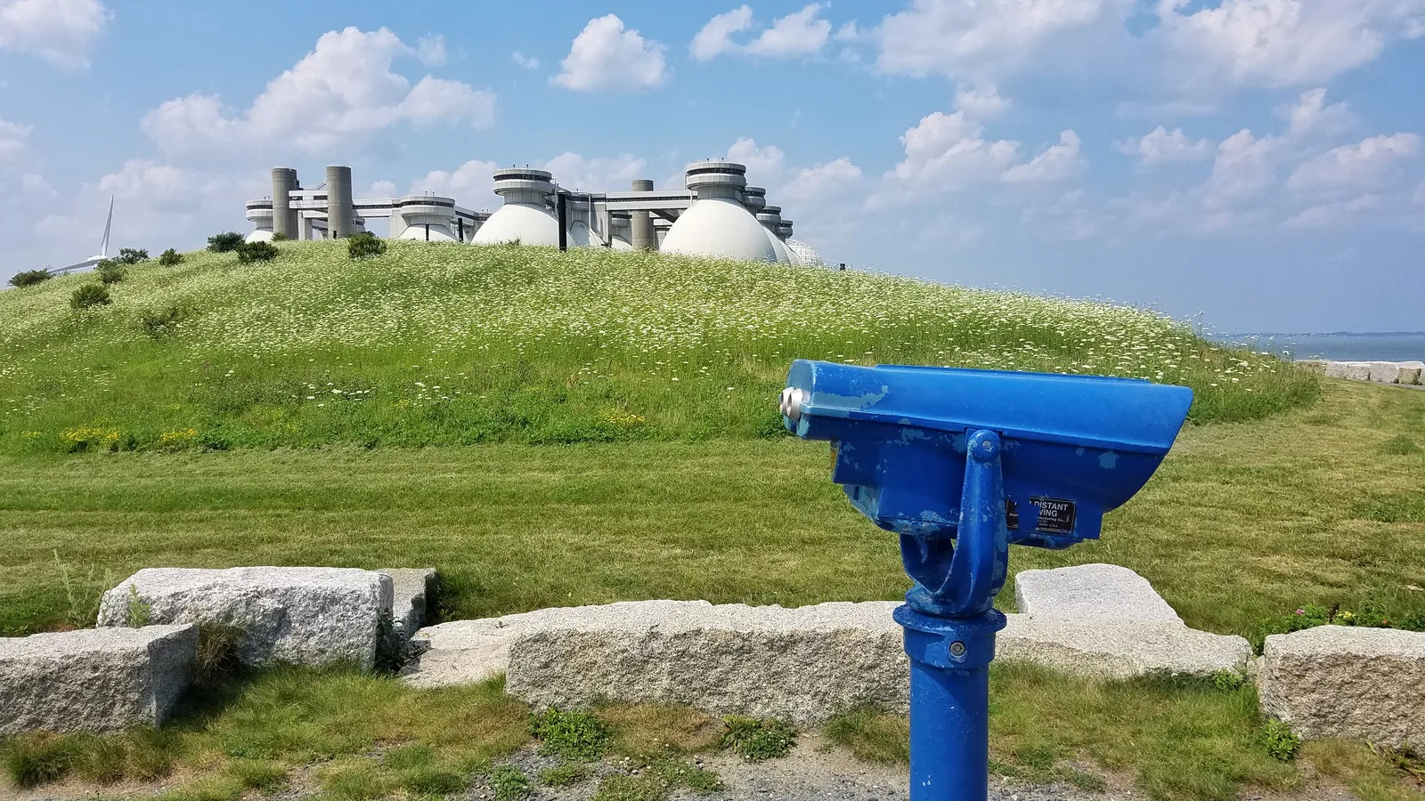 Large round treatment tanks and service roads extend across a wastewater plant beside the harbor.