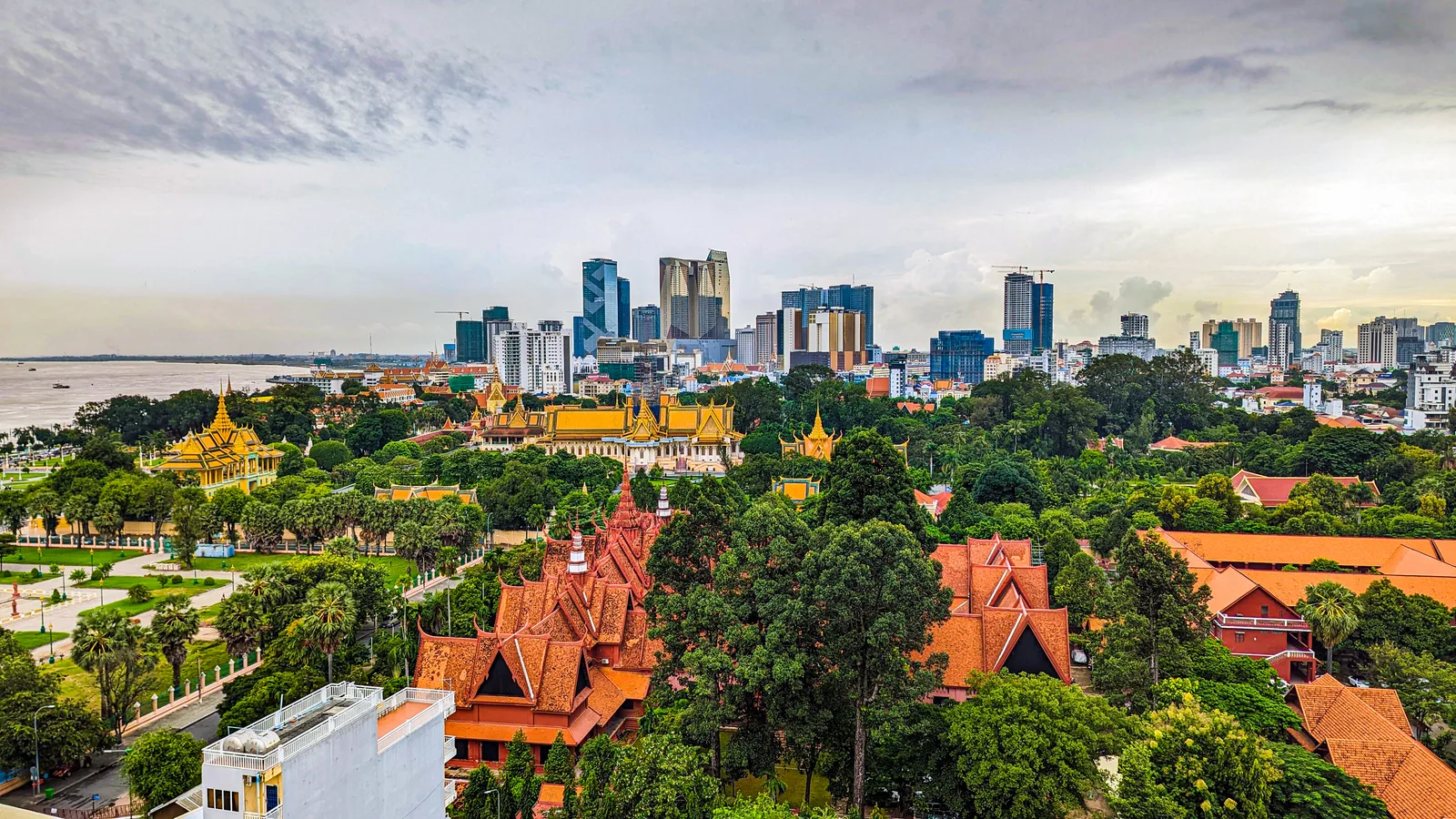 The Phnom Penh skyline stretches beyond the Royal Palace and riverfront under a hazy sky.