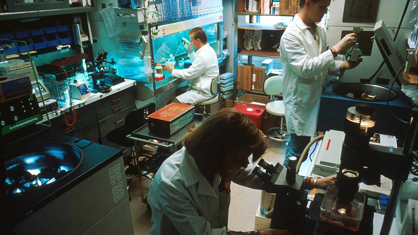 Three scientists work among benches and equipment in a cancer research laboratory.