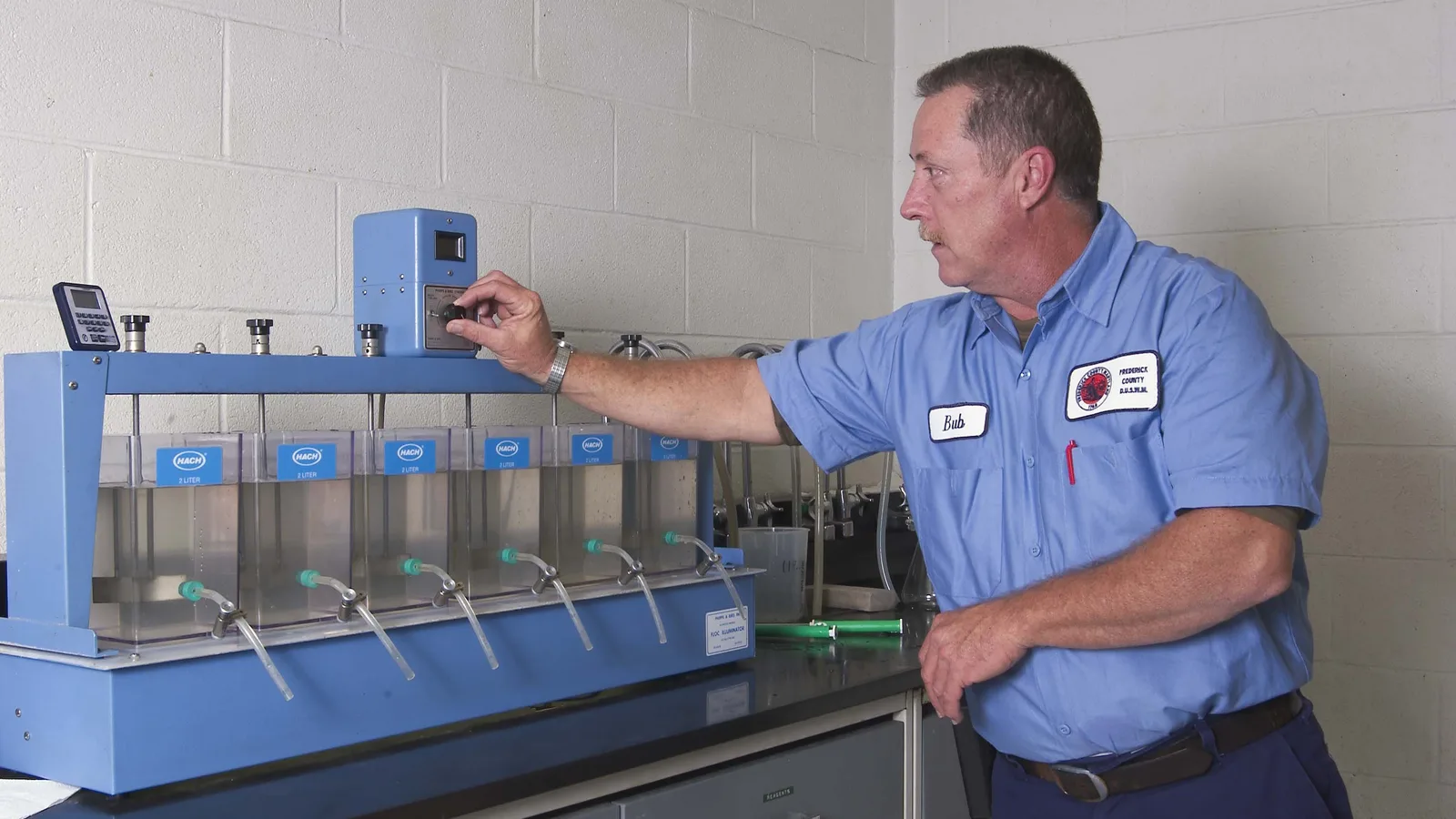 A water-treatment operator examines rows of beakers during a jar test.